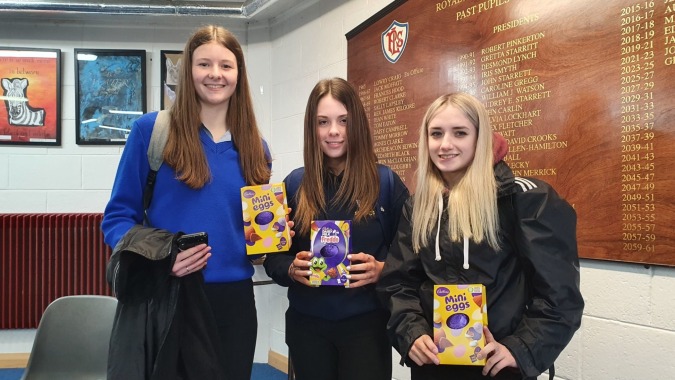 Drei Schülerinnen stehen im Flur der Royal & Prior Comprehensive School und halten Snacks in der Hand.