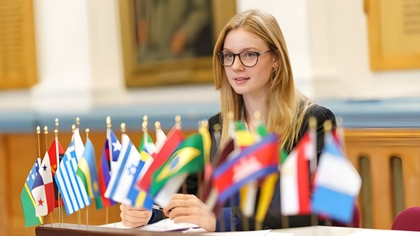 Eine junge Frau mit Brille steht vor einer Ausstellung internationaler Flaggen auf dem Gelände der Royal Russell School.