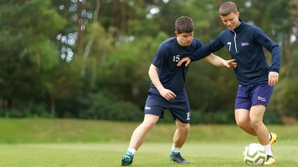 Zwei Schüler der Royal Russell School spielen Fußball auf einem Rasenplatz umgeben von Bäumen.