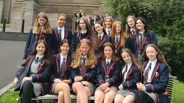 Eine Gruppe junger Schülerinnen in Schuluniform sitzt auf einer Bank vor einem historischen Gebäude der Royal School Armagh.