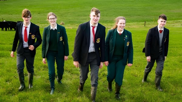 Schüler der Royal School Cavan stehen auf einem grasbewachsenen Feld mit Kühen im Hintergrund.