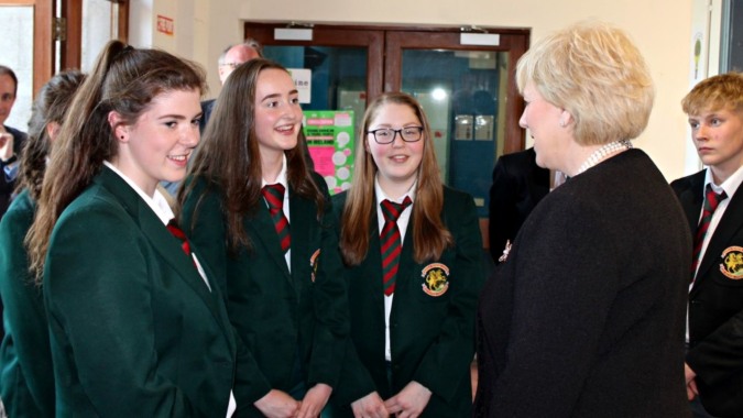 Eine Gruppe von Schülerinnen und Schülern der Royal School Cavan unterhält sich im Schulflur in Schuluniformen mit grünen und schwarzen Roben.