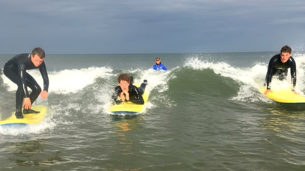 Schüler der Royal School Cavan surfen im Neoprenanzug auf Wellen im Ozean bei bewölktem Himmel.