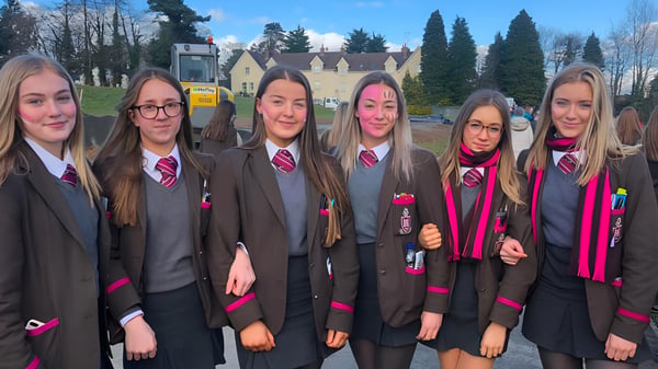 Eine Gruppe Schülerinnen in Hogwarts-ähnlichen Uniformen steht vor einer malerischen Kulisse auf dem Campus der Royal School Dungannon.