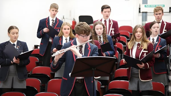 Eine Gruppe Schüler in Uniformen der Royal School sitzt mit Notenblättern in einem Vortragsraum mit roten Stühlen.
