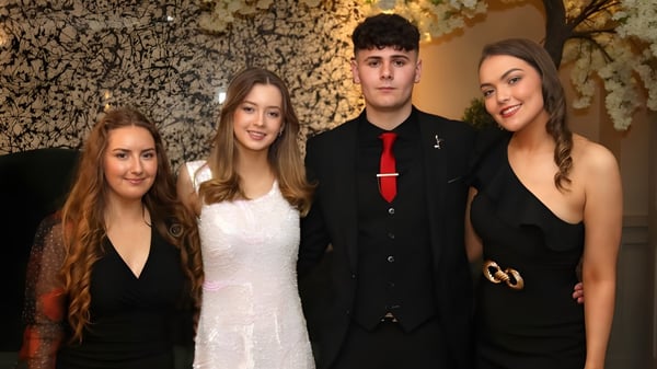 Vier Schülerinnen und Schüler der Royal School posieren in formeller Kleidung vor einer strukturierten Steinwand.