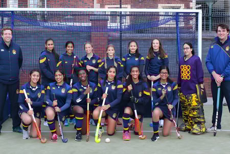 Eine Gruppe junger Sportlerinnen posiert auf dem Sportplatz der Royal School Wolverhampton vor einem Backsteingebäude.