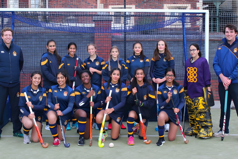 Eine Gruppe junger Sportlerinnen posiert auf dem Sportplatz der Royal School Wolverhampton vor einem Backsteingebäude.