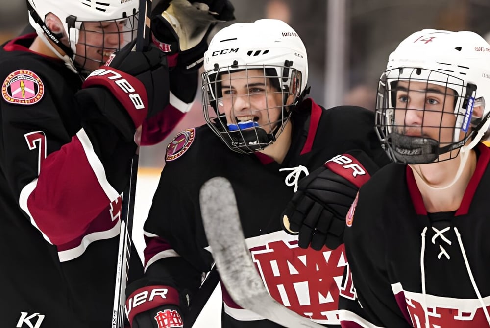 Drei Eishockeyspieler in Uniform auf dem Eis, einer trägt ein Trikot mit den Buchstaben A und M, auf dem Eisfeld der Royal Vale High School.