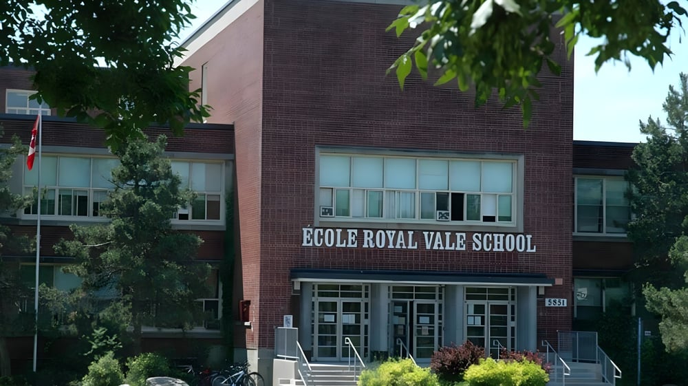 Das Backsteingebäude der Royal Vale High School mit einem Schild ist von grünen Bäumen umgeben.