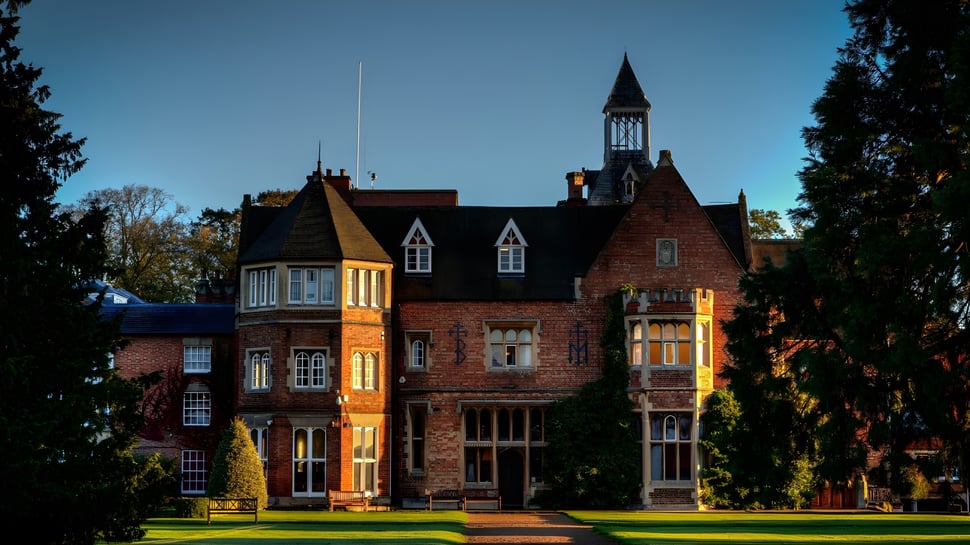 Das historische Backsteingebäude der Rugby School mit hohem Turm steht umgeben von grünem Laub.