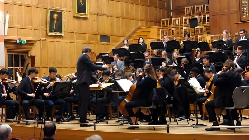 Das Orchester der Rugby School spielt auf einer Bühne in einem großen Konzertsaal mit Holzvertäfelung.