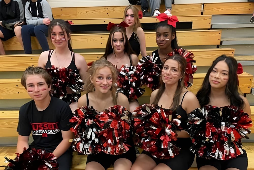 Eine Gruppe Cheerleader der Russell High School posiert gemeinsam auf einer Holzbühne vor Zuschauern.