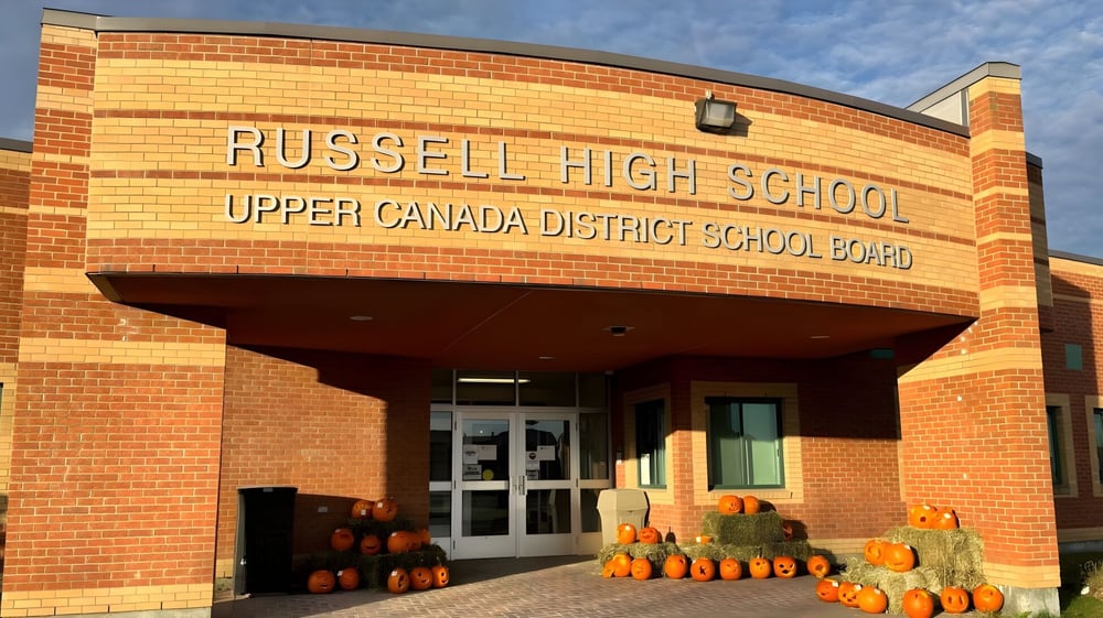 Der Eingang von Russell High School mit einem Schild des Upper Canada District School Board und einer Pumpkin-Dekoration im Vordergrund.