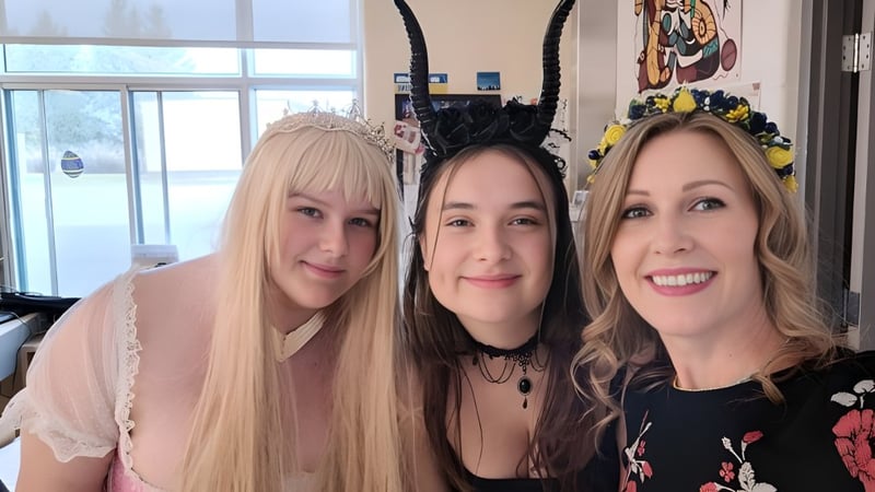 Drei lächelnde Frauen mit unterschiedlicher Haarfarbe posieren vor einem farbenfrohen Wandgemälde in der Russell High School.