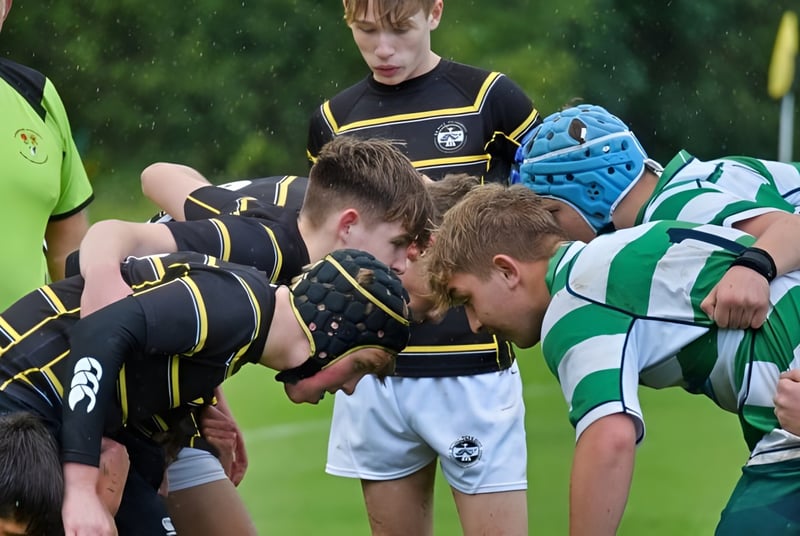 Eine Gruppe von rugbyspielenden Schülerinnen und Schülern der Rydal Penrhos School ist beim Scrum auf dem Rasenfeld zu sehen.
