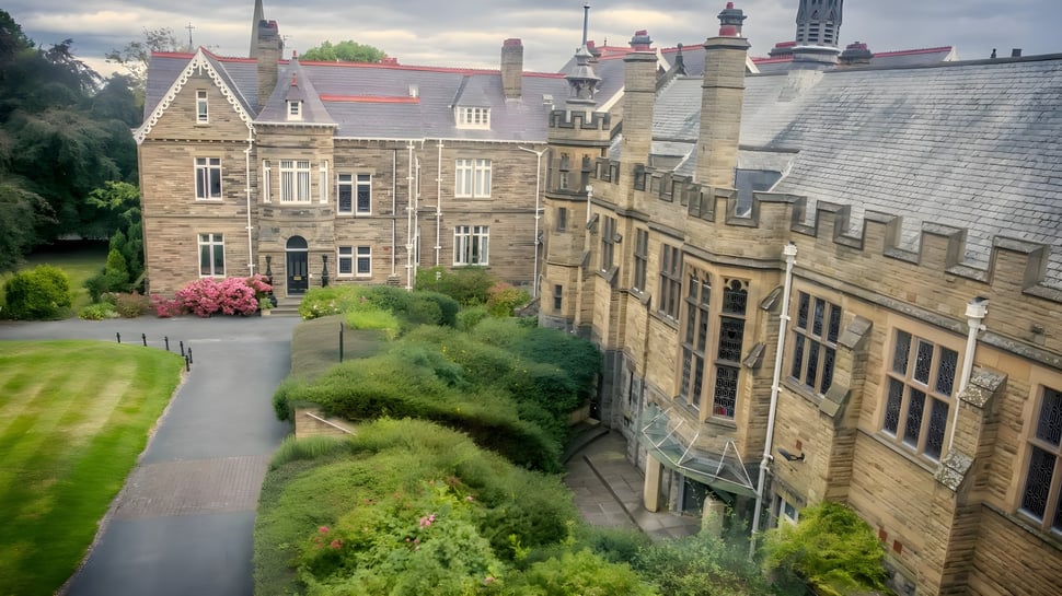 Das mittelalterlich gestaltete Hauptgebäude der Rydal Penrhos School umgeben von grüner Bepflanzung und einem gewundenen Weg.