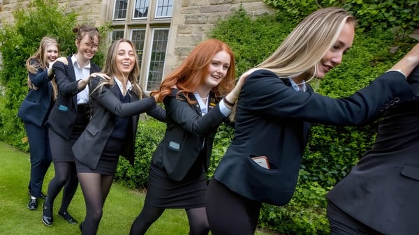 Eine Gruppe junger Schülerinnen in schwarzen Anzügen steht vor dem steinernen Gebäude der Rydal Penrhos School umgeben von grüner Landschaft.