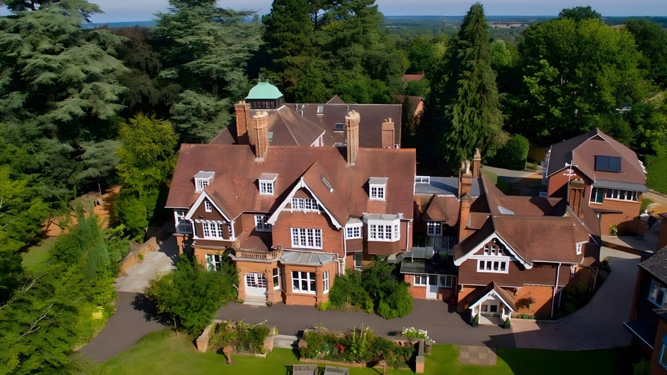 Das historische Herrenhaus mit kupferner Kuppel auf dem Gelände der Rye St. Antony School ist von grüner Vegetation umgeben.
