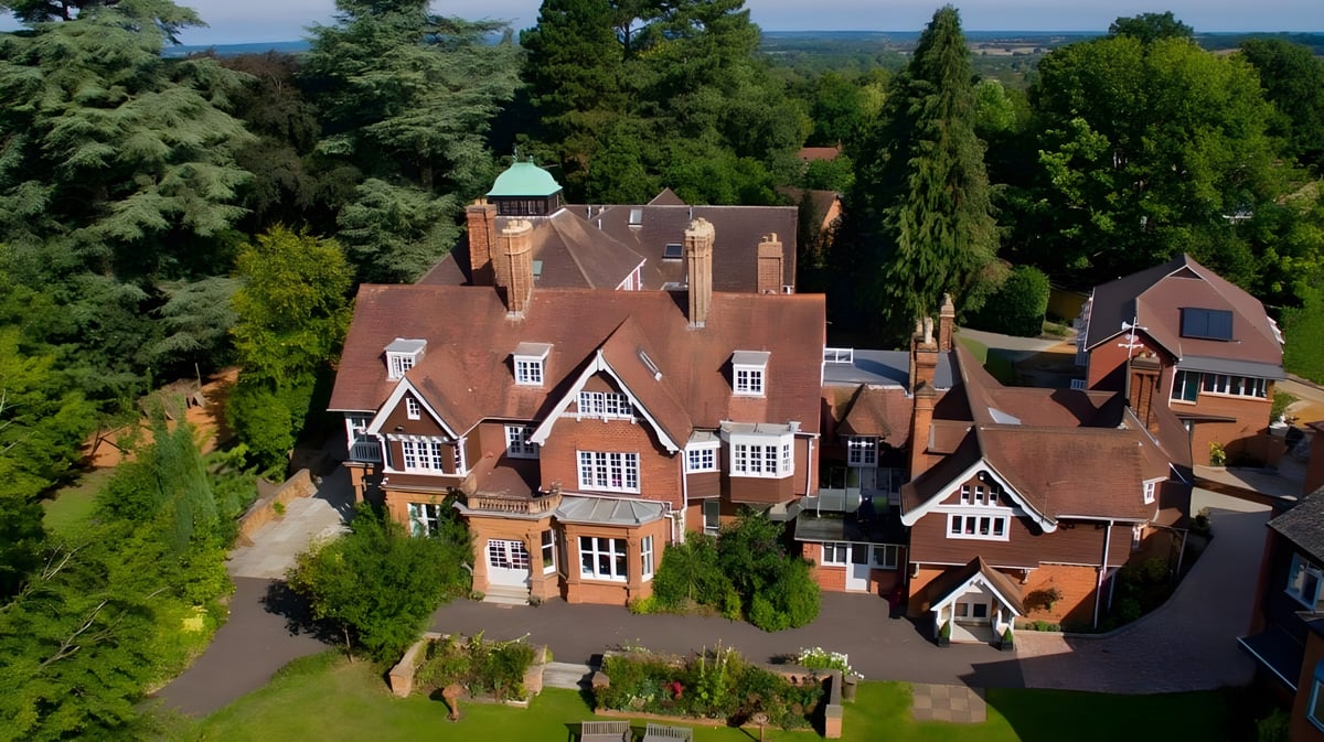 Das historische Herrenhaus mit kupferner Kuppel auf dem Gelände der Rye St. Antony School ist von grüner Vegetation umgeben.
