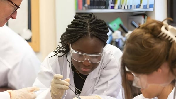 Eine Schülerin in einem weißen Kittel untersucht eine andere Schülerin mit geflochtenen Haaren in einem Labor der Rye St. Antony School.