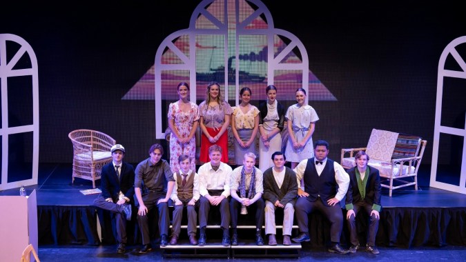 Eine Gruppe von Schülerinnen und Schülern steht auf der Bühne des Sacred Heart College vor einem farbenfrohen, verzierten Hintergrund.