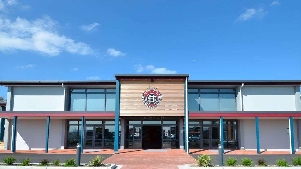 Das moderne mehrstöckige Gebäude mit einem großen Emblem an der Fassade des Sacred Heart College Napier vor blauem Himmel.