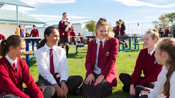 Schülerinnen und Schüler des Sacred Heart College Napier sitzen im Freien auf dem Gras vor einem Schulgebäude.