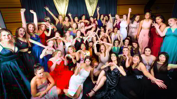 Eine Gruppe von Schülerinnen des Sacred Heart College Napier posiert feierlich in formeller Kleidung mit erhobenen Armen.