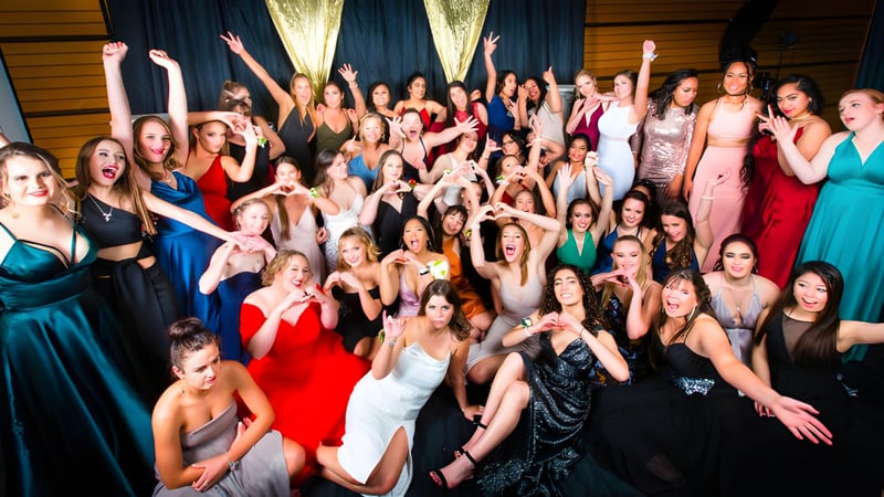 Eine Gruppe von Schülerinnen des Sacred Heart College Napier posiert feierlich in formeller Kleidung mit erhobenen Armen.