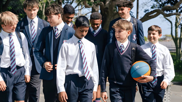 Eine Gruppe Schülerinnen und Schüler des Sacred Heart College steht in Schuluniformen draußen vor Bäumen und Gebäuden.