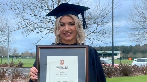 Eine Absolventin hält in der Abschlussrobe auf dem Gelände des Sacred Heart Girls' College in Hamilton ihr Diplom und lächelt.