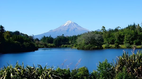 Ein ruhiger See mit grüner Ufervegetation und schneebedecktem Berg im Hintergrund in der Nähe des Sacred Heart Girls' College in New Plymouth.