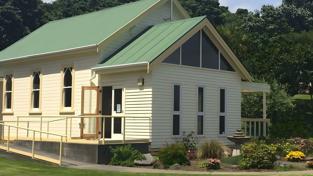 Ein charmantes Holzhaus mit grünem Metalldach steht inmitten von Bäumen und einem gepflegten Garten auf dem Gelände des Sacred Heart Girls' College in New Plymouth.