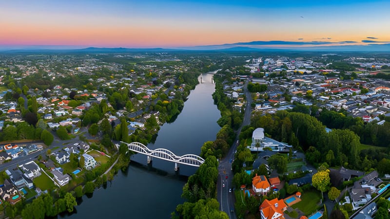 Luftaufnahme einer Stadt an einem Fluss mit grünen Bergen im Hintergrund bei Sonnenuntergang.