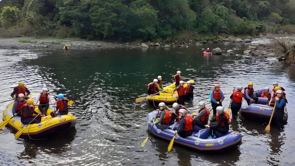 Schülerinnen des Sacred Heart Girls' College in New Plymouth beim Rafting auf einem Fluss mit grüner Umgebung.