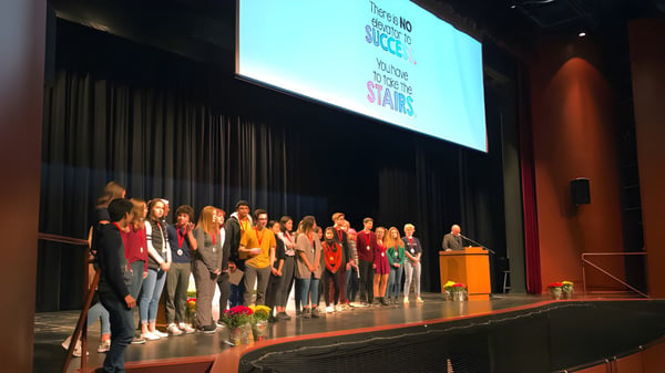 Schüler der Sacred Heart High School stehen auf der Bühne vor einer großen Projektionswand mit Text.