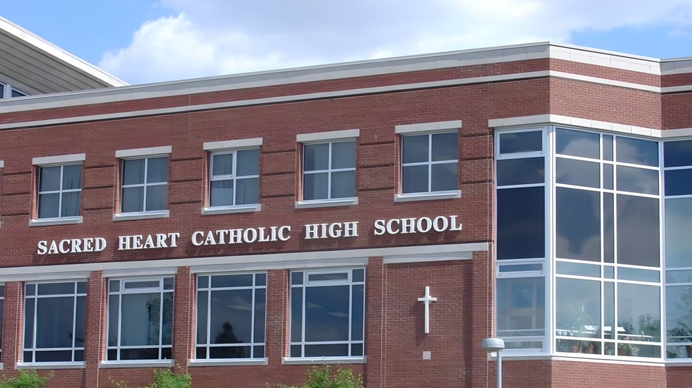 Das große Backsteingebäude der Sacred Heart High School ist unter einem klaren blauen Himmel mit Wolken zu sehen.