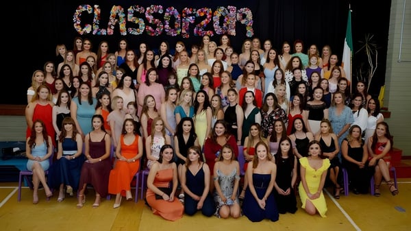 Eine große Gruppe Schülerinnen der Sacred Heart School posiert in bunten Kleidern in einer Sporthalle vor dem Schriftzug CLASSOF2020.