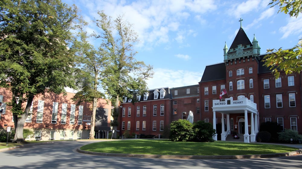 Das Backsteingebäude mit Uhrturm auf dem Campus der Sacred Heart School of Halifax ist von Bäumen und gepflegtem Rasen umgeben.