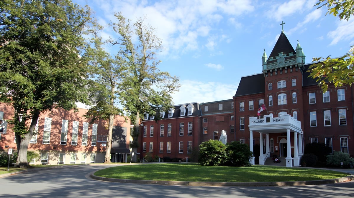 Das Backsteingebäude mit Uhrturm auf dem Campus der Sacred Heart School of Halifax ist von Bäumen und gepflegtem Rasen umgeben.