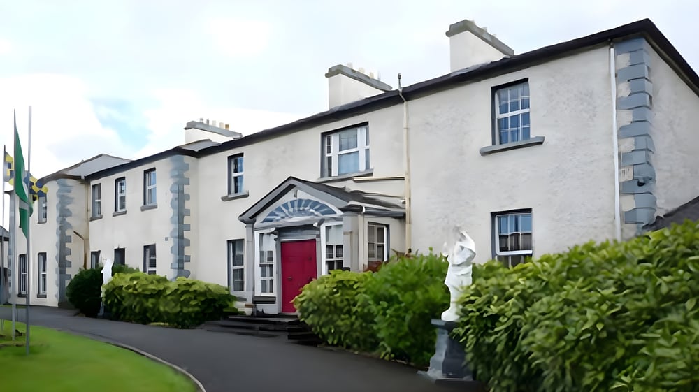 Das mehrstöckige Gebäude der Sacred Heart School mit roter Tür ist von grünen Bäumen und einer Grasfläche umgeben.