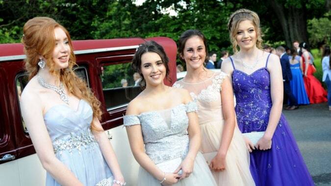 Vier Schülerinnen der Sacred Heart Secondary School Clonakilty posieren vor einem roten Oldtimer in einem grünen Umfeld.