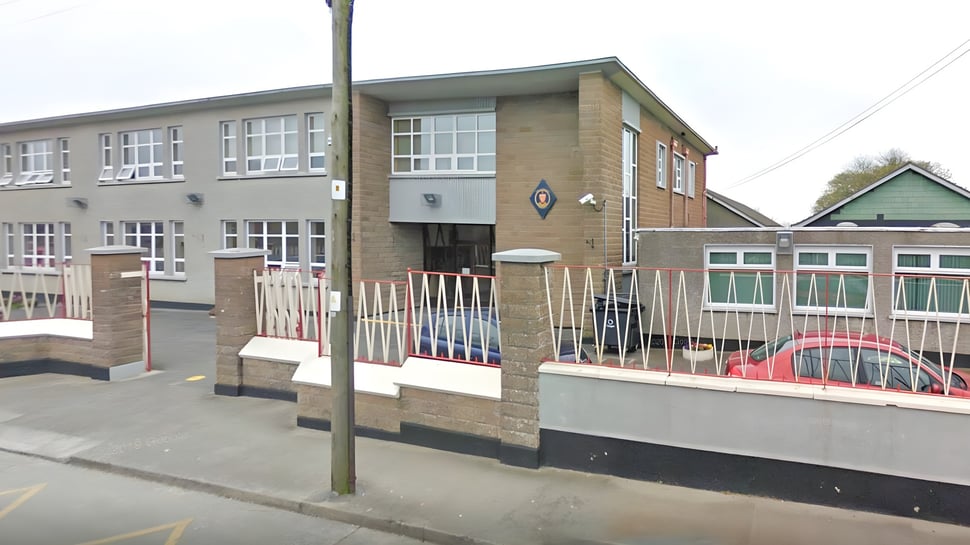 Das mehrstöckige Backsteingebäude der Sacred Heart Secondary School in Drogheda mit großen Fenstern und umzäuntem Bereich im Vordergrund.