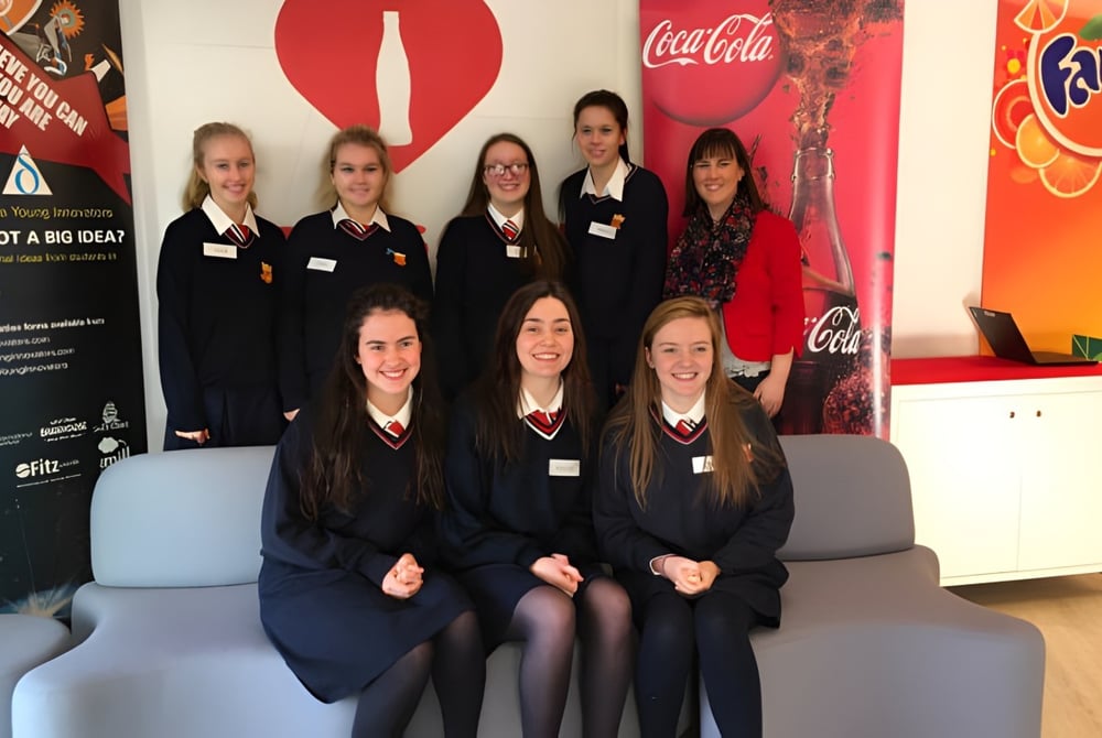 Eine Gruppe von Schülerinnen der Sacred Heart Secondary School in Drogheda posiert vor Coca-Cola- und Fanta-Werbehintergründen.