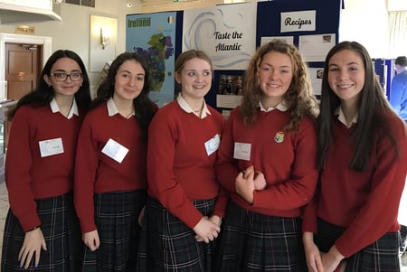 Fünf Schülerinnen der Sacred Heart Secondary School Clonakilty stehen zusammen im Schulflur vor bunten Plakaten.