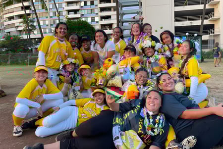 Eine Gruppe von Schülerinnen der Sacred Hearts Academy versammelt sich draußen vor Gebäuden mit Palmen im Hintergrund.