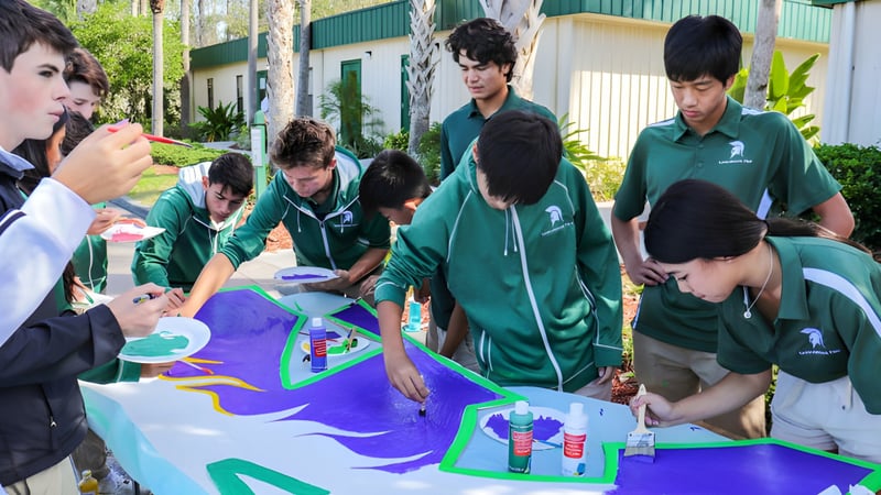 Schüler der Saddlebrook Preparatory School arbeiten gemeinsam an einem großen bunten Kunstprojekt auf einem Tisch.