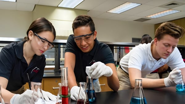 Drei Schüler der Sagemont School führen im Labor wissenschaftliche Experimente mit Schutzkleidung durch.