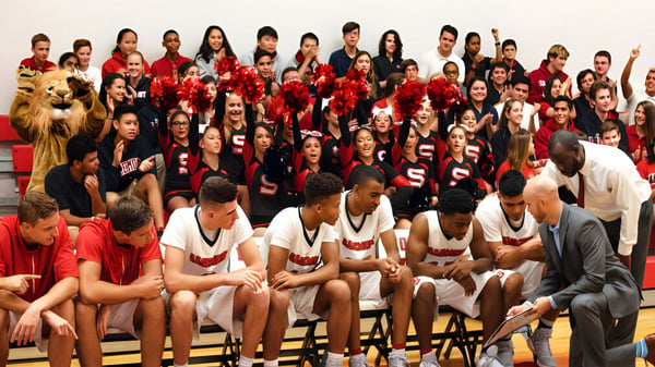 Eine Gruppe Schülerinnen und Schüler der Sagemont School versammelt sich in einer Sporthalle in roten und weißen Uniformen.